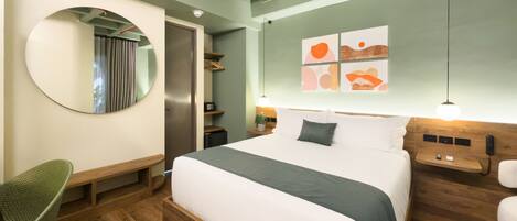 A modern hotel room with a large bed, a round mirror, a desk, and a wardrobe.
