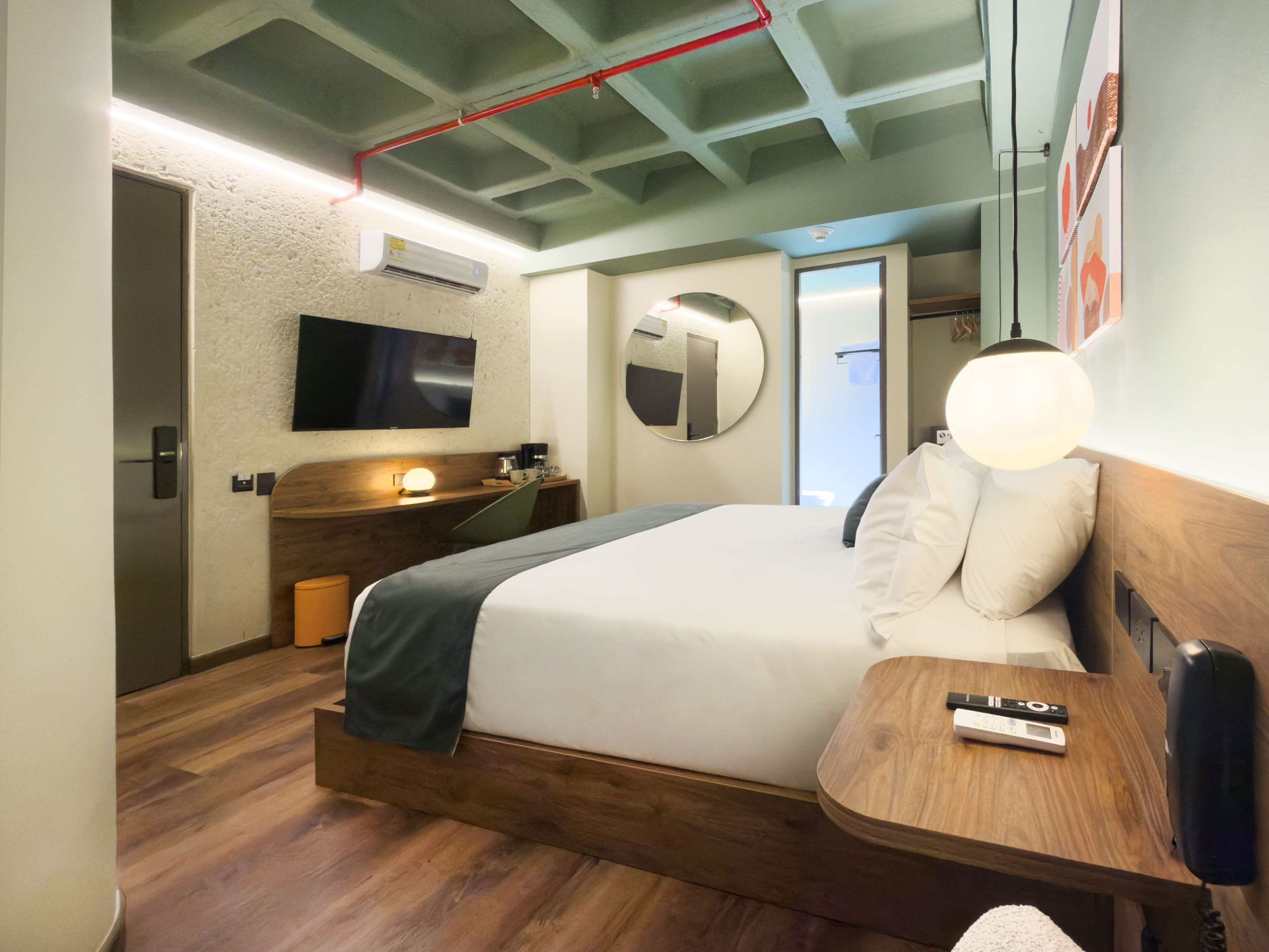 Une chambre d’hôtel équipée d’un lit, d’une table de chevet, d’une lampe, d’un miroir et d’un téléviseur fixé au mur.