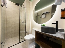 A modern bathroom with a glass-enclosed shower, a round mirror, a black sink, and a toilet.