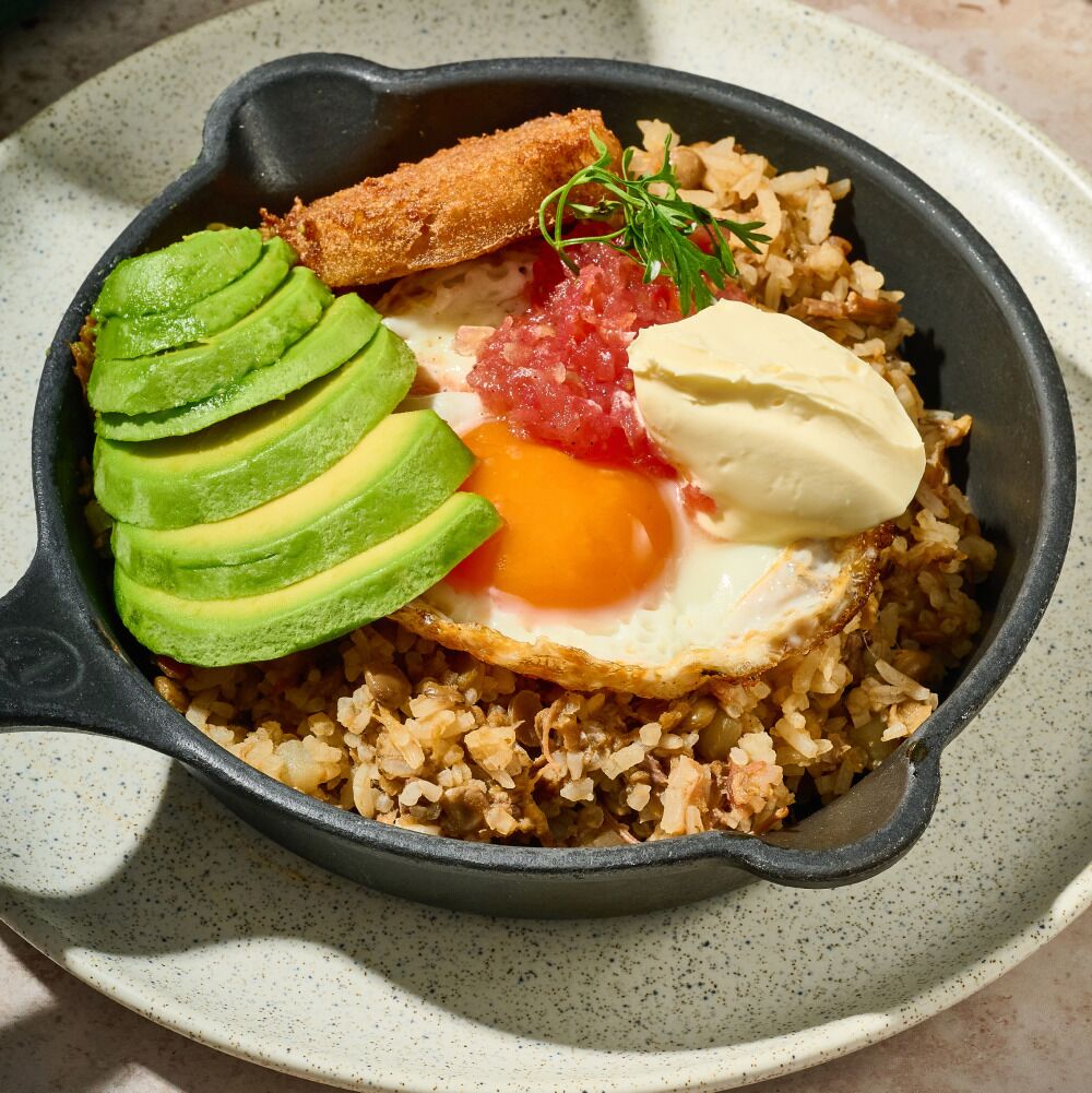 A skillet with fried rice, avocado slices, a fried egg, and a piece of bread.