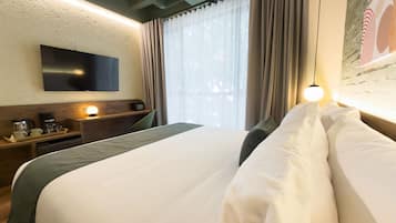 Quarto de hotel com cama, televisão de tela plana na parede, cafeteira e janela com cortinas.