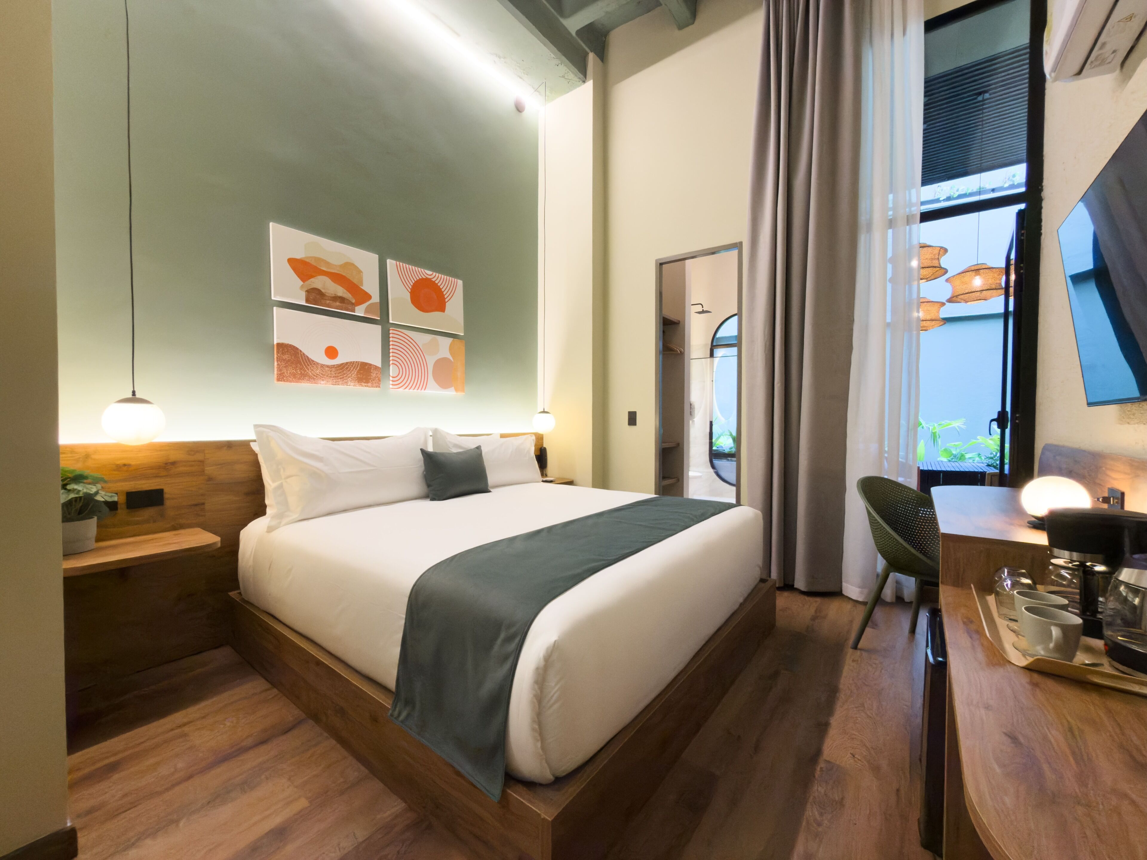 A modern hotel room with a large bed, bedside tables, a desk with a chair, and artwork on the wall.
