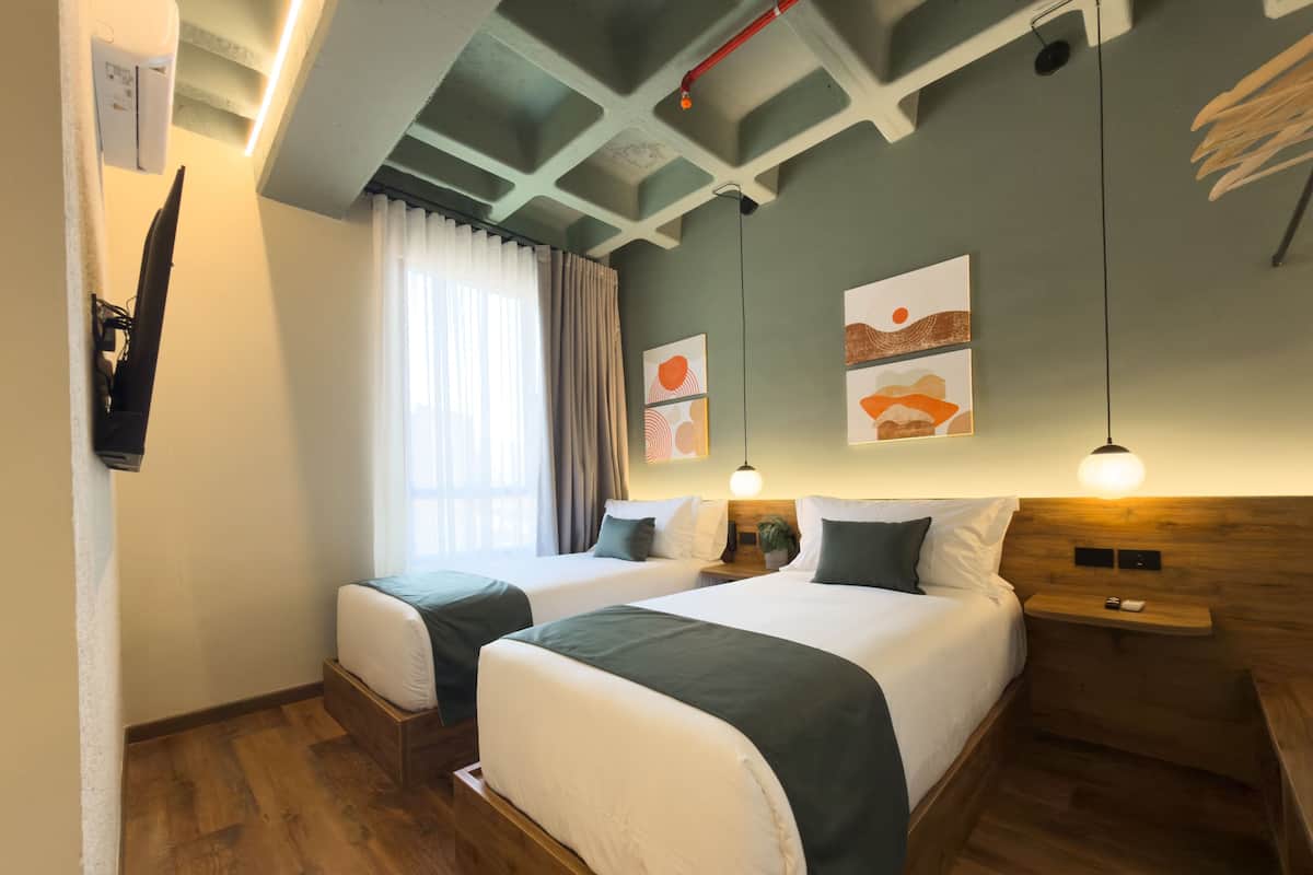 Habitación de hotel con dos camas, piso de madera, techo con vigas a la vista y obras de arte en las paredes.