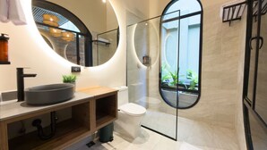 A modern bathroom with a round mirror, a sink, a toilet, and a glass-enclosed shower.