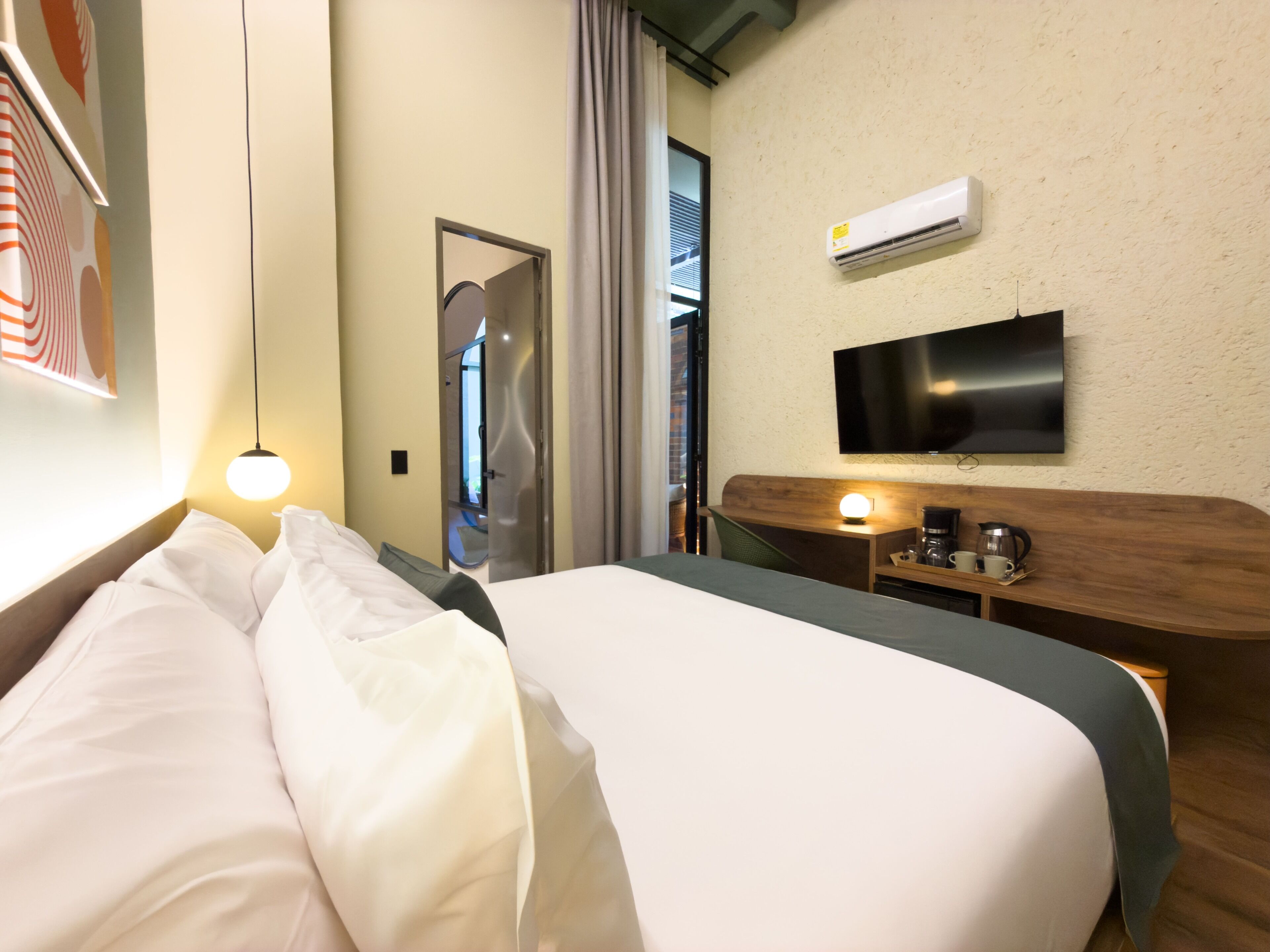 Een hotelkamer met een bed, een bureau met een flatscreen televisie, een airconditioningsysteem en een raam met gordijnen.