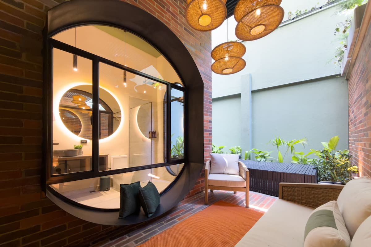 Un interior moderno con un ventanal circular, una zona de estar con un banco acolchado y una pequeña mesa.