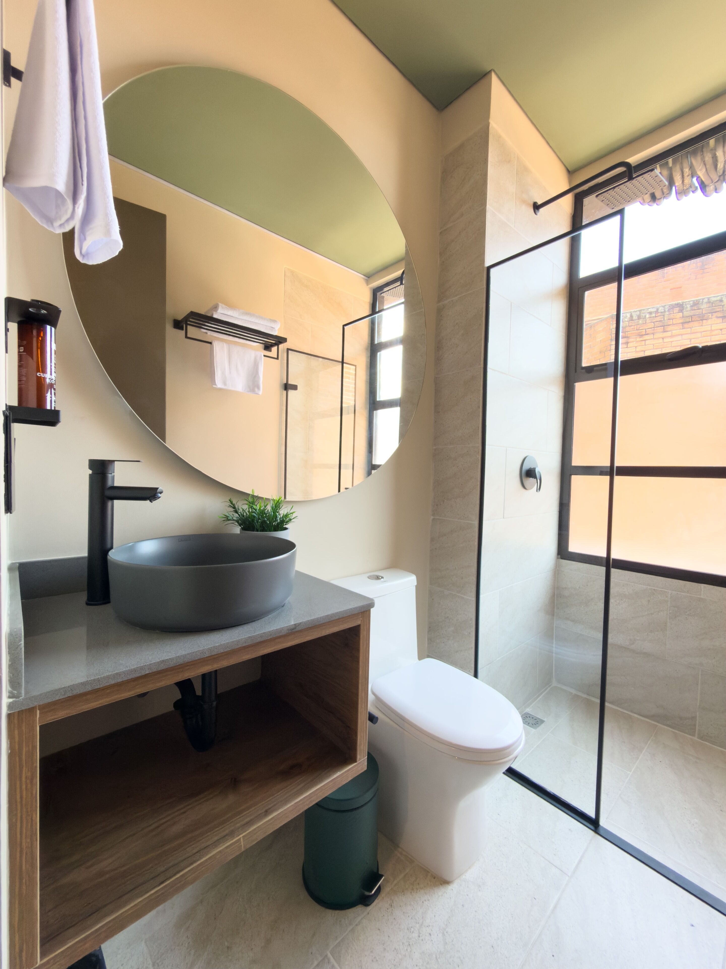 A modern bathroom with a round sink, a toilet, a shower with glass doors, and a large mirror.
