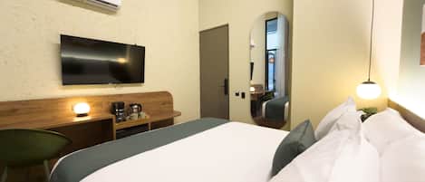 A hotel room with a bed, a television, a coffee maker, a mirror, and an air conditioning unit.