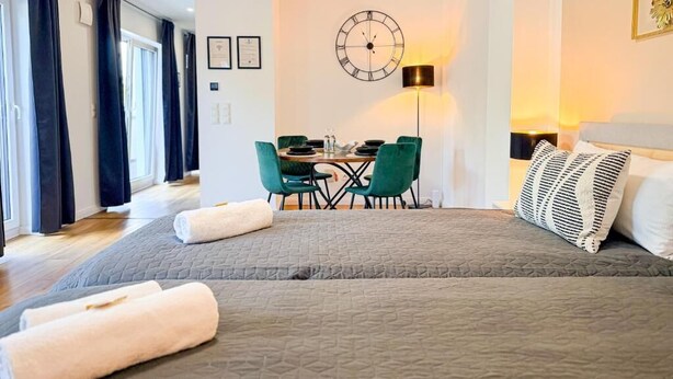 Hotellihuone, jossa on suuri sänky, ruokapöytä tuoleineen, seinäkello ja lamppu.