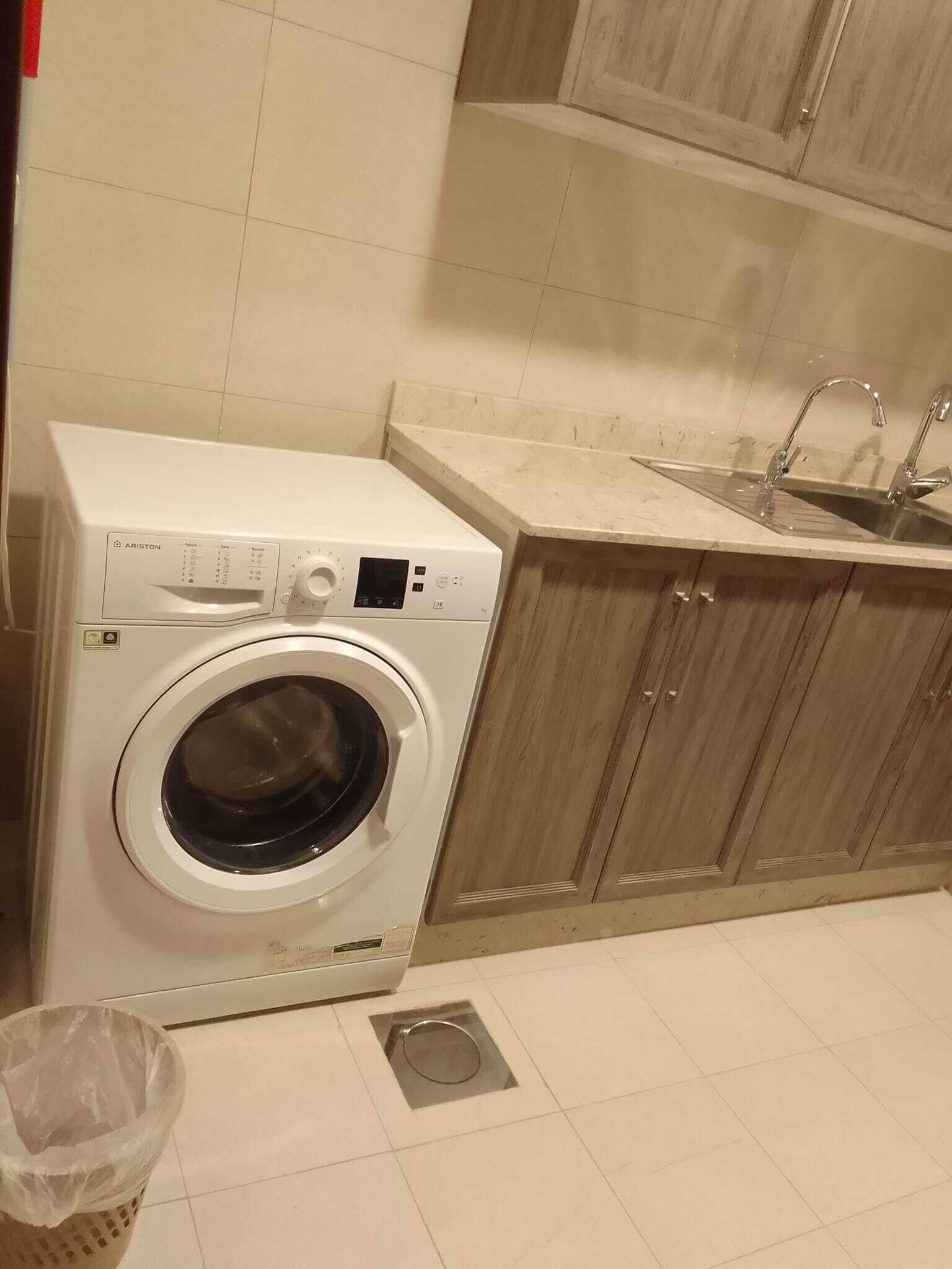 Una lavadora compacta en una cocina pequeña con un lavabo y armarios de madera.