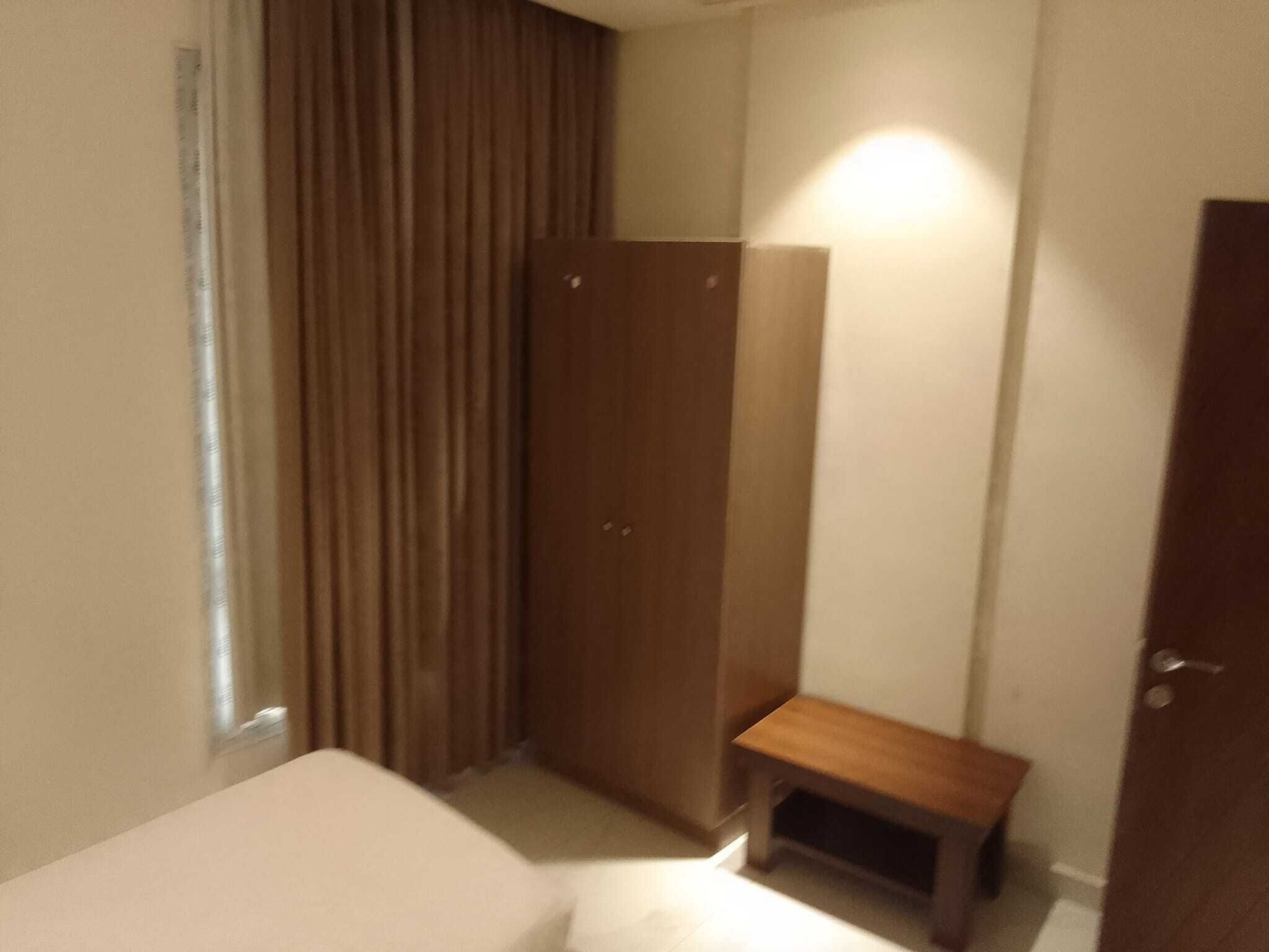 A bedroom with a bed, a wooden wardrobe, a small bench, and a door.