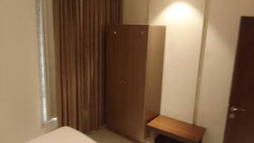 A bedroom with a bed, a wooden wardrobe, a small bench, and a door.