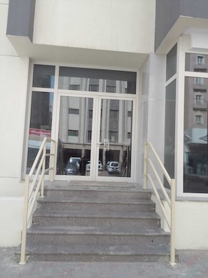 Une entrée d’immeuble avec un escalier en béton menant à une porte en verre.