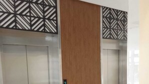 Un pasillo con dos ascensores, uno con paneles de madera y otro con paneles metálicos.