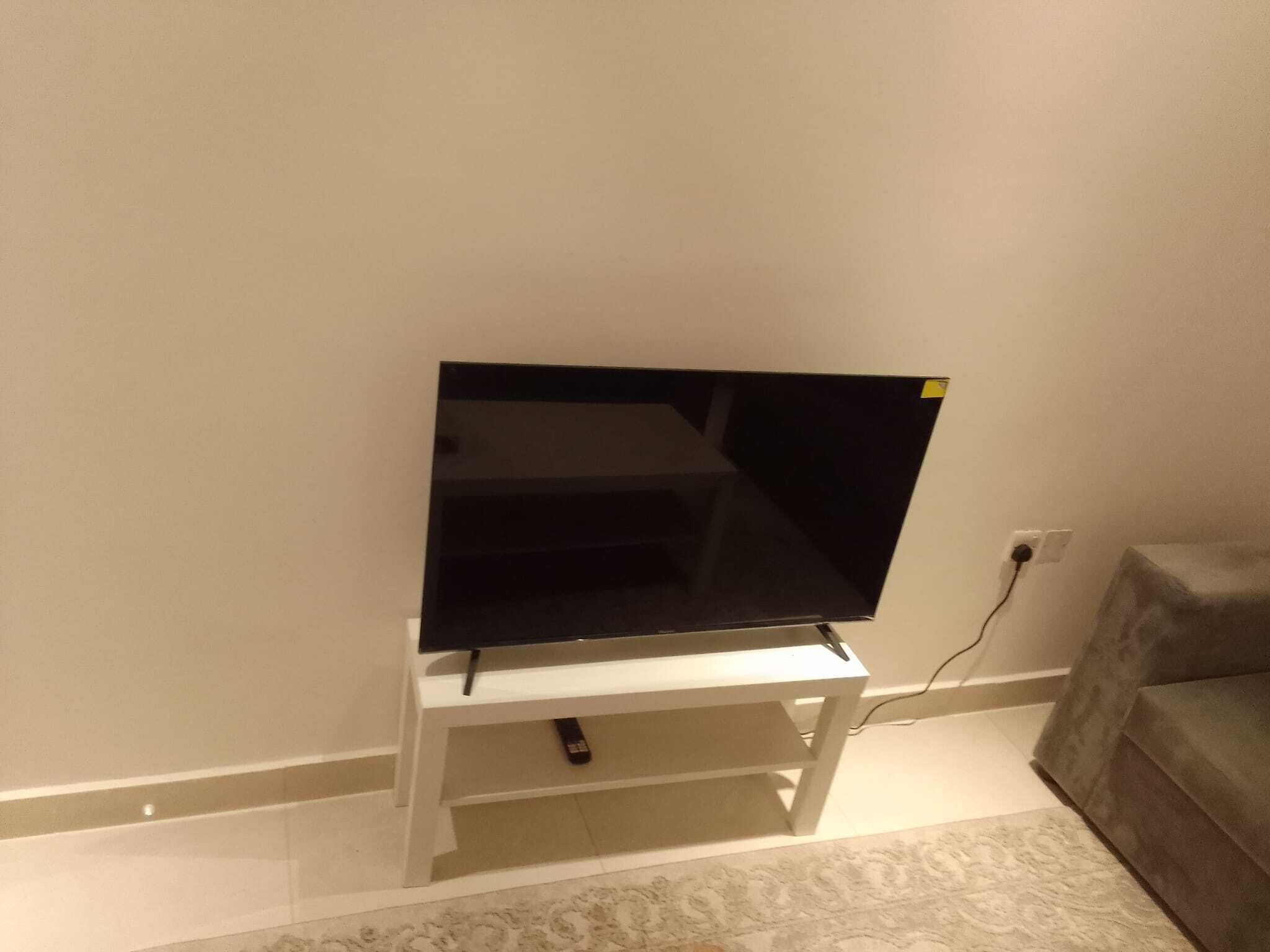 Un téléviseur à écran plat, posé sur un meuble blanc, avec une télécommande à proximité.
