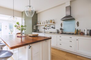 Une cuisine moderne dotée d’un îlot central en bois, de luminaires suspendus, d’une hotte en acier inoxydable et de meubles de rangement blancs.