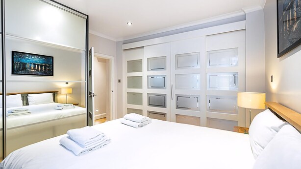 A hotel room with a bed, a mirror, a wardrobe with multiple doors, and a painting on the wall. - Marylebone Boutique Retreat (London)