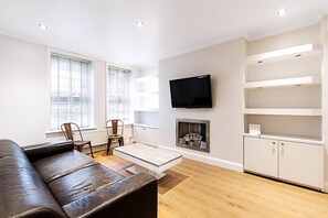 Ein modernes Wohnzimmer mit einer Couch, einem an der Wand befestigten Fernseher, einem Kamin und eingebauten Regalen.