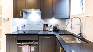 A modern kitchen with dark cabinets, a black countertop, a stainless steel sink, and a built-in oven. - Marylebone Boutique Retreat (London)