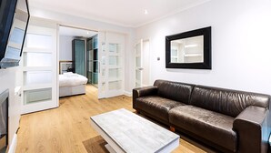 A modern living room with a brown leather sofa, a white coffee table, and a TV mounted on the wall. - Marylebone Boutique Retreat (London)