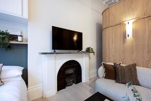 Ein modernes Wohnzimmer mit einem flachbildfernseher über einem Kamin, einer Couch mit Kissen und einer kleinen Pflanze auf dem Kaminvorsatz.