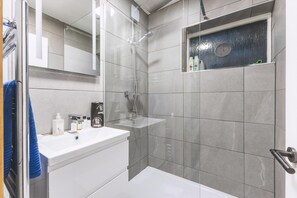 A modern bathroom with a glass-enclosed shower, a white sink, and a mirror. - Bright Islington One Bedroom Retreat (London)