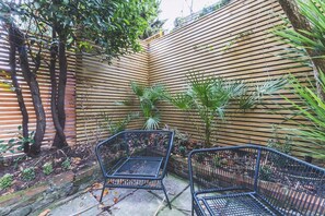 Ein Gartenbereich mit einer Holzwand, zwei Metallstühlen und verschiedenen Pflanzen.