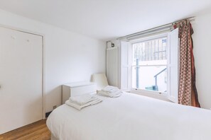 Ein Schlafzimmer mit Bett, Heizkörper, einem Fenster mit Vorhängen und einer Tür.