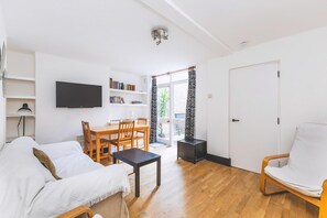 A living room with a sofa, a dining table with chairs, a TV mounted on the wall, a bookshelf, and a door leading to an outdoor area. - Bright Islington One Bedroom Retreat (London)