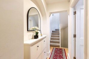 A hallway with a white vanity, a mirror, a red and white patterned rug, and a staircase leading to a landing. - Elegant Pimlico Townhouse (London)