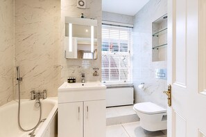 A bathroom with a bathtub, a sink, a toilet, and a window with blinds. - Elegant Pimlico Townhouse (London)