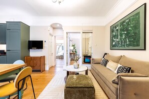 Un salon moderne avec un canapé, un pouf et un téléviseur.