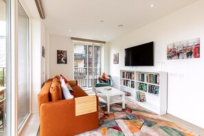 Ein modernes Wohnzimmer mit einer Couch, einem Couchtisch, einem Bücherregal und einem an der Wand befestigten Fernseher.