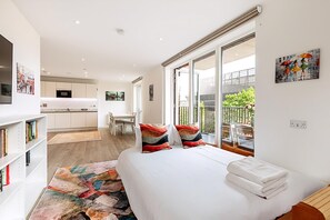 A modern hotel room with a large bed, a view of the balcony, a dining area, and a kitchen. - Stratford Flat Near Abba Arena (London)