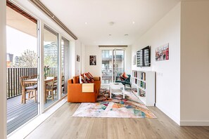A modern living room with a sofa, coffee table, and a bookshelf. - Stratford Flat Near Abba Arena (London)