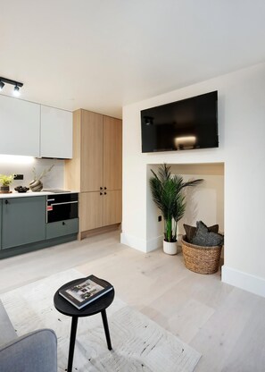 Eine moderne Küche mit hellen Holzschränken, einem eingebauten Backofen und einem flachbildfernseher an der Wand.
