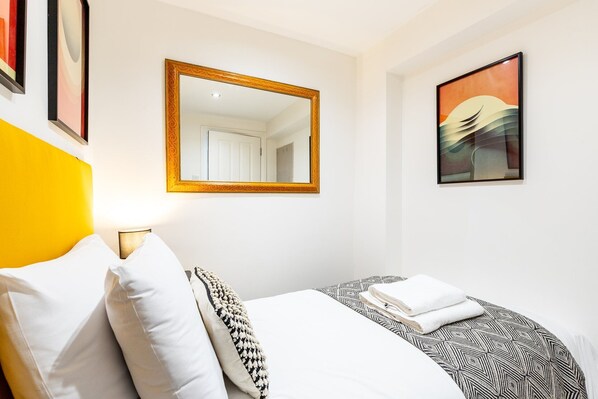 A hotel room with a bed, a mirror, and artwork on the walls. - Snug Holland Park Stay (London)