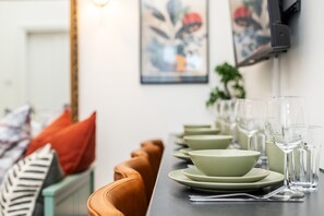 A dining table set with green plates, bowls, and clear glasses, with a sofa and cushions in the background. - Snug Holland Park Stay (London)