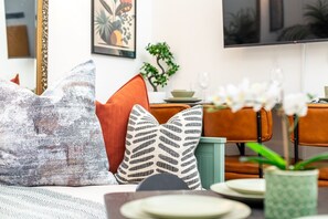Ein Wohnzimmer mit einer Couch, Kissen, einem Couchtisch, einem Fernseher und einer Pflanze.