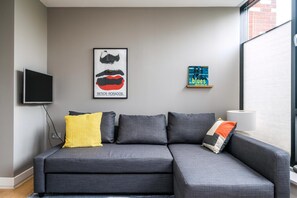 Ein graues Sofa mit vielen Kissen, ein flachbildschirm-Fernseher an der Wand und zwei gerahmte Kunstwerke.