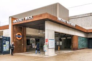 Ein Bahnhofseingang mit der Beschilderung 'Hackney Wick', einer Übersichtstafel und einem Fahrkartengerät.