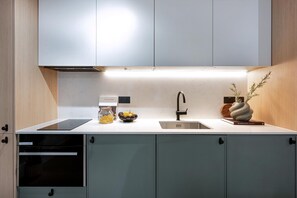 Eine moderne Küche mit eingebautem Geschirrspüler, einer Spüle und einer Arbeitsplatte, auf der sich ein Pastaglas, eine Obstschale und eine dekorative Vase befinden.