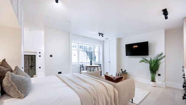 Ein modernes Schlafzimmer mit einem großen Bett, einem Fernseher, einer Pflanze und Blick ins Freie.