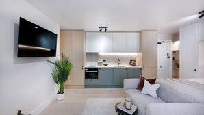 Ein modernes Wohnzimmer mit einem Flachbildfernseher, einem grauen Sofa, einem kleinen Beistelltisch und einer Topfpflanze.