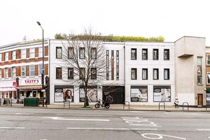 Straßenansicht mit einem Restaurant namens 'Tasty's' auf der linken Seite, einem Gebäude mit Baum davor und einem abgestellten Fahrrad.