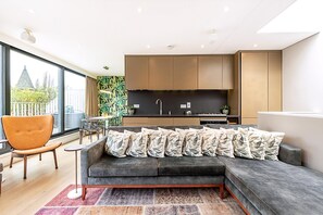 Ein modernes Wohnzimmer mit grauem Sofa, einem orangefarbenen Sessel und einer Küchenzeile mit Holzschränken und einer schwarzen Arbeitsplatte.