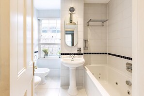 Ein Badezimmer mit einem Standwaschbecken, einer Toilette, einer Badewanne und einem Fenster mit Blick auf Gebäude.