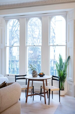 Ein Zimmer mit einem runden Tisch, zwei Stühlen, einer Topfpflanze und einer Heizung.