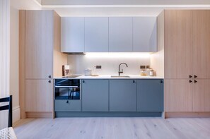 Eine moderne Küche mit hellen Holzschränken, einem eingebauten Backofen und einer Spüle aus Edelstahl.