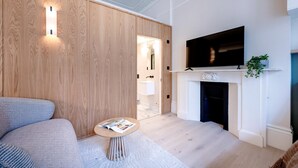 Un soggiorno moderno con un divano, un tavolino rotondo, una TV a schermo piatto sopra un caminetto e una parete in legno con illuminazione integrata.